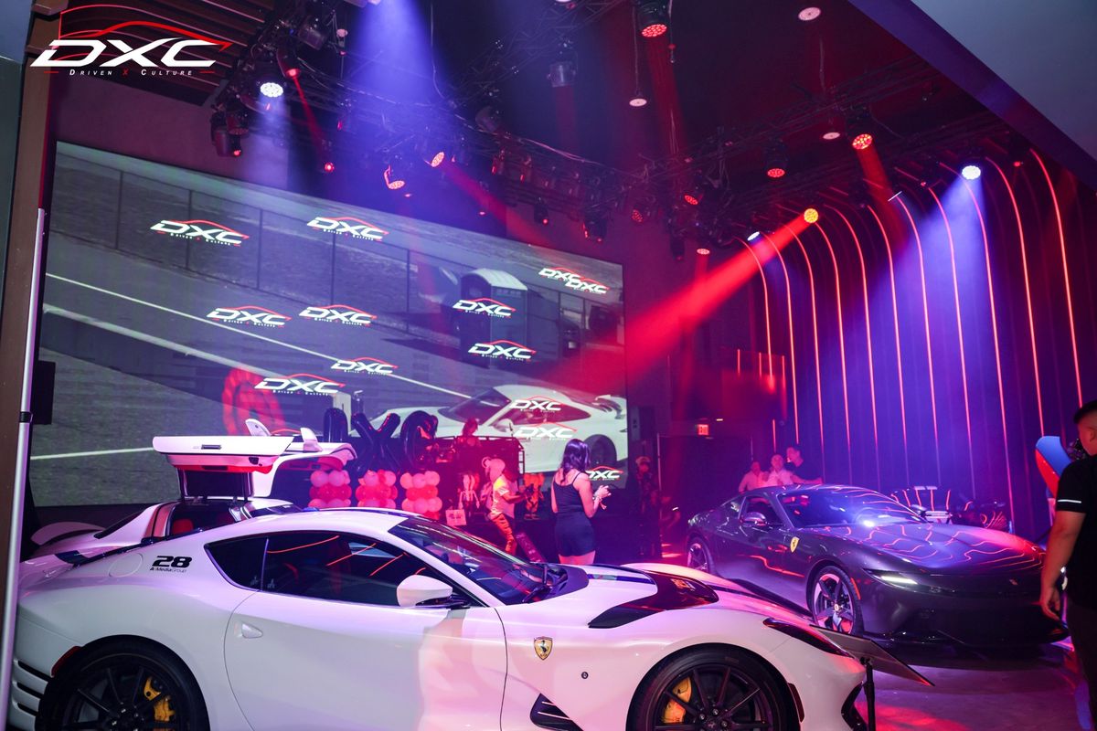 A white and a grey Ferrari under red and purple stage lights in front of the DXC screen